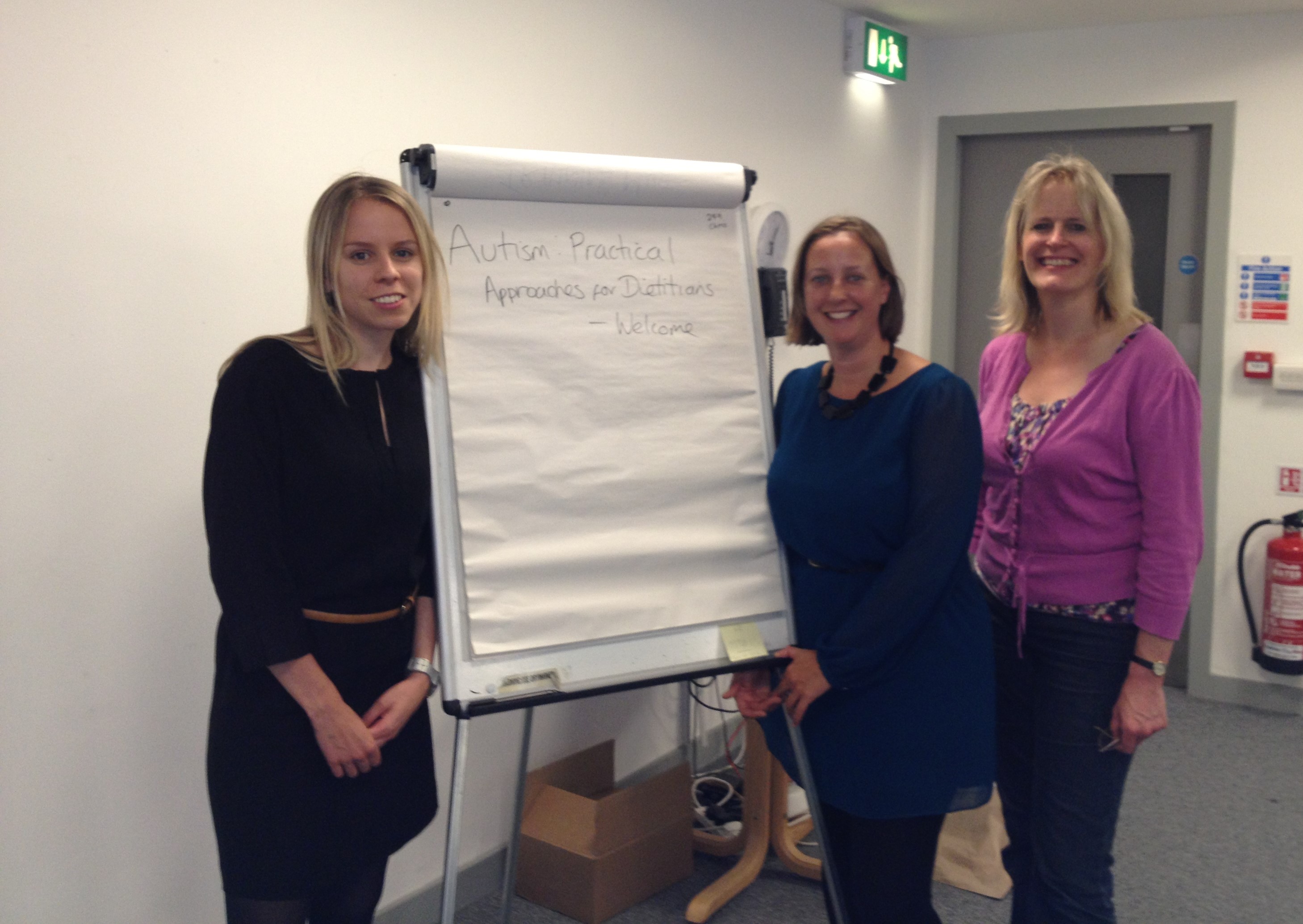 Photograph of 3 white women stood infront of a Flipchart