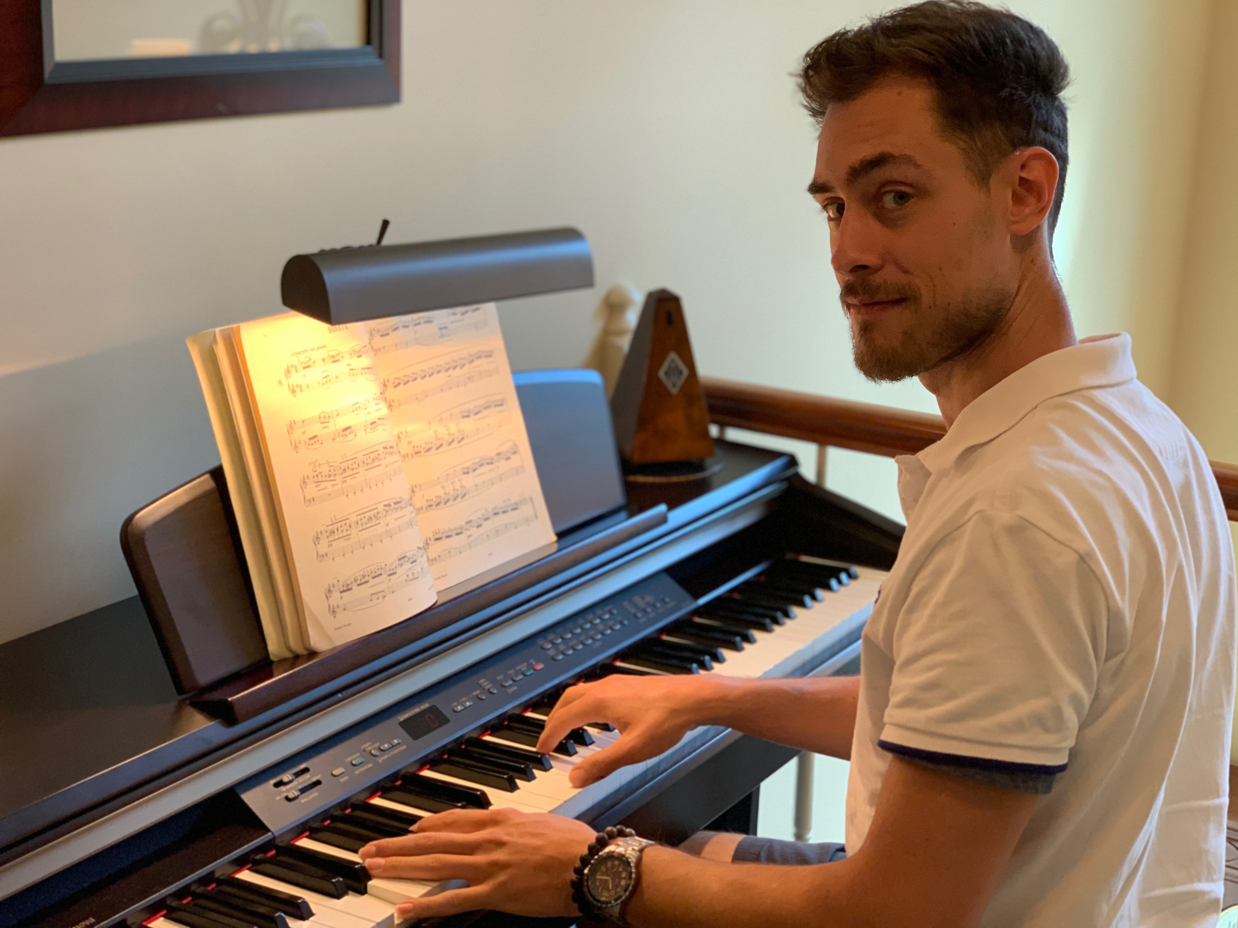 Aaron Neuhaus Looking at the Camera While Playing on an Electric Piano with Sheet Music on the Music Stand