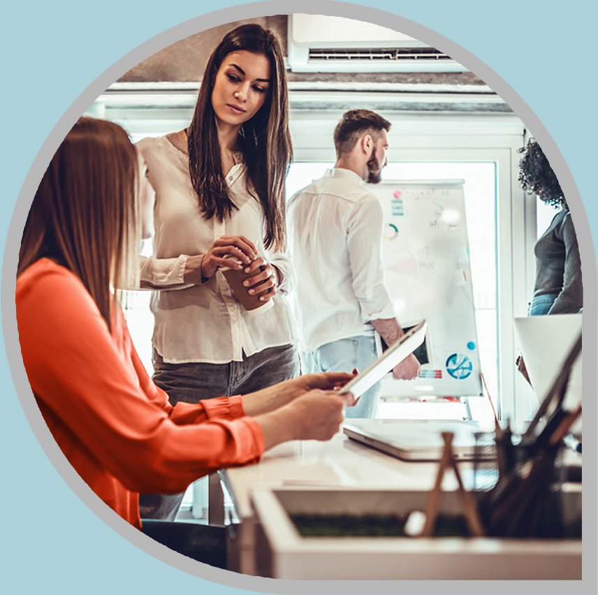 Two coworking women asking questions in a busy workspace