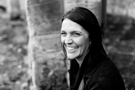 Black and white head and shoulders image of a smiling lady with long dark hair and a leather jacket