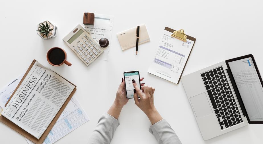 Young woman holding phone and doing numbers while managing her business. Photo by rawpixel 