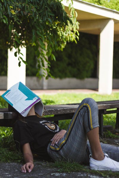 Tired student napping with textbook resting on face