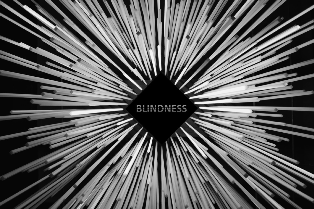 An abstract picture with shafts of white light being sucked into a central black diamond which has the word 'Blindness' written on it