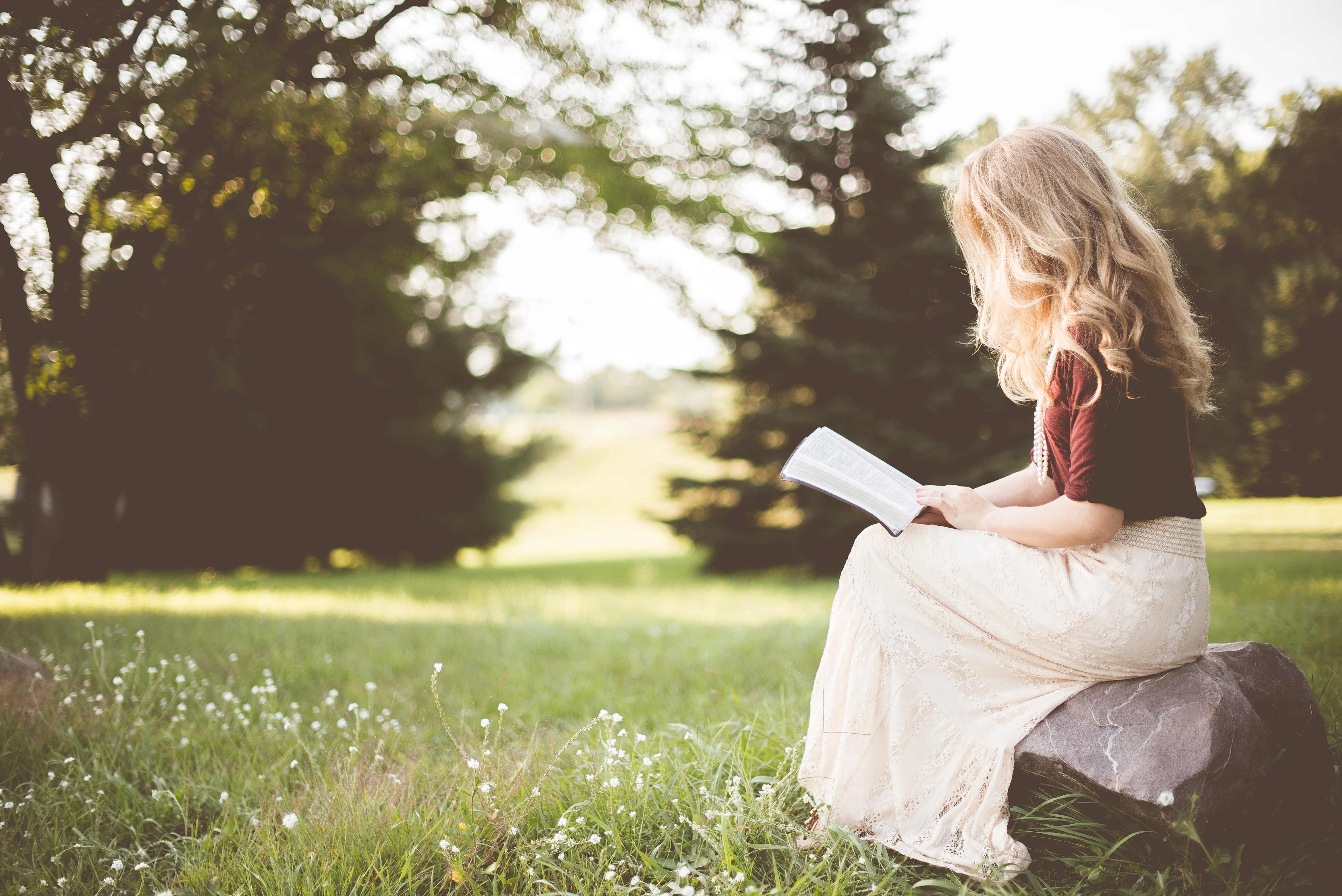 woman reading Bible sitting on a rock