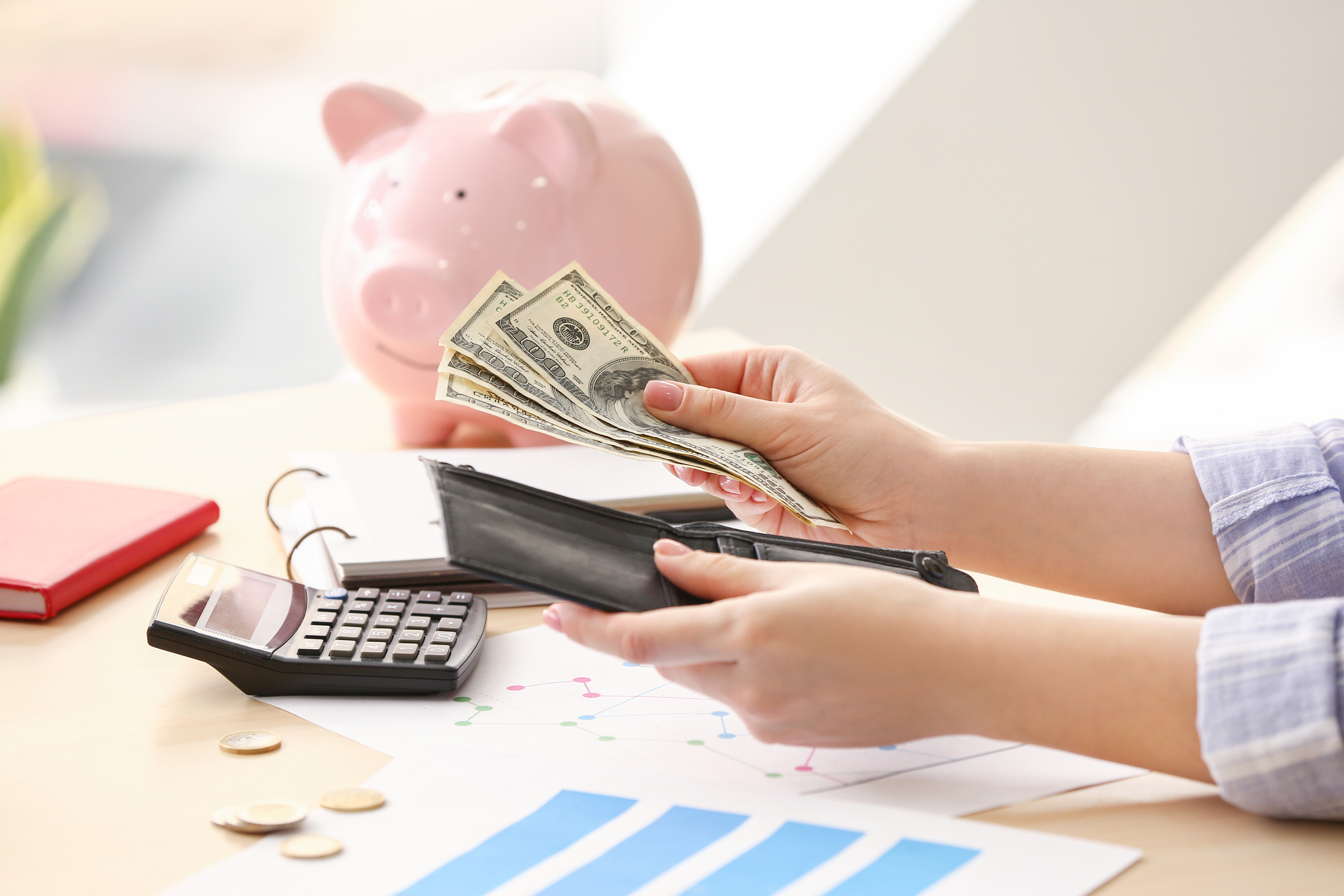 female hands counting dollar bills from open purse with notebook and calculator in background