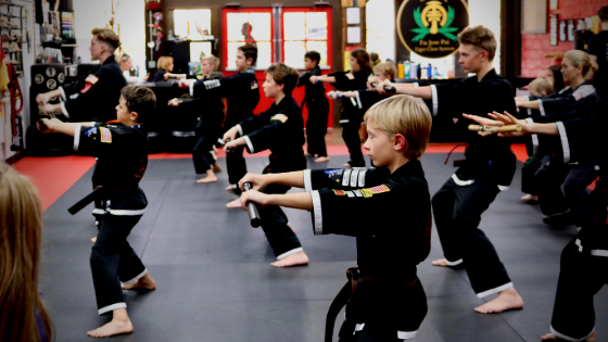 junior martial arts students in horse stance with arms out holding nunchucks