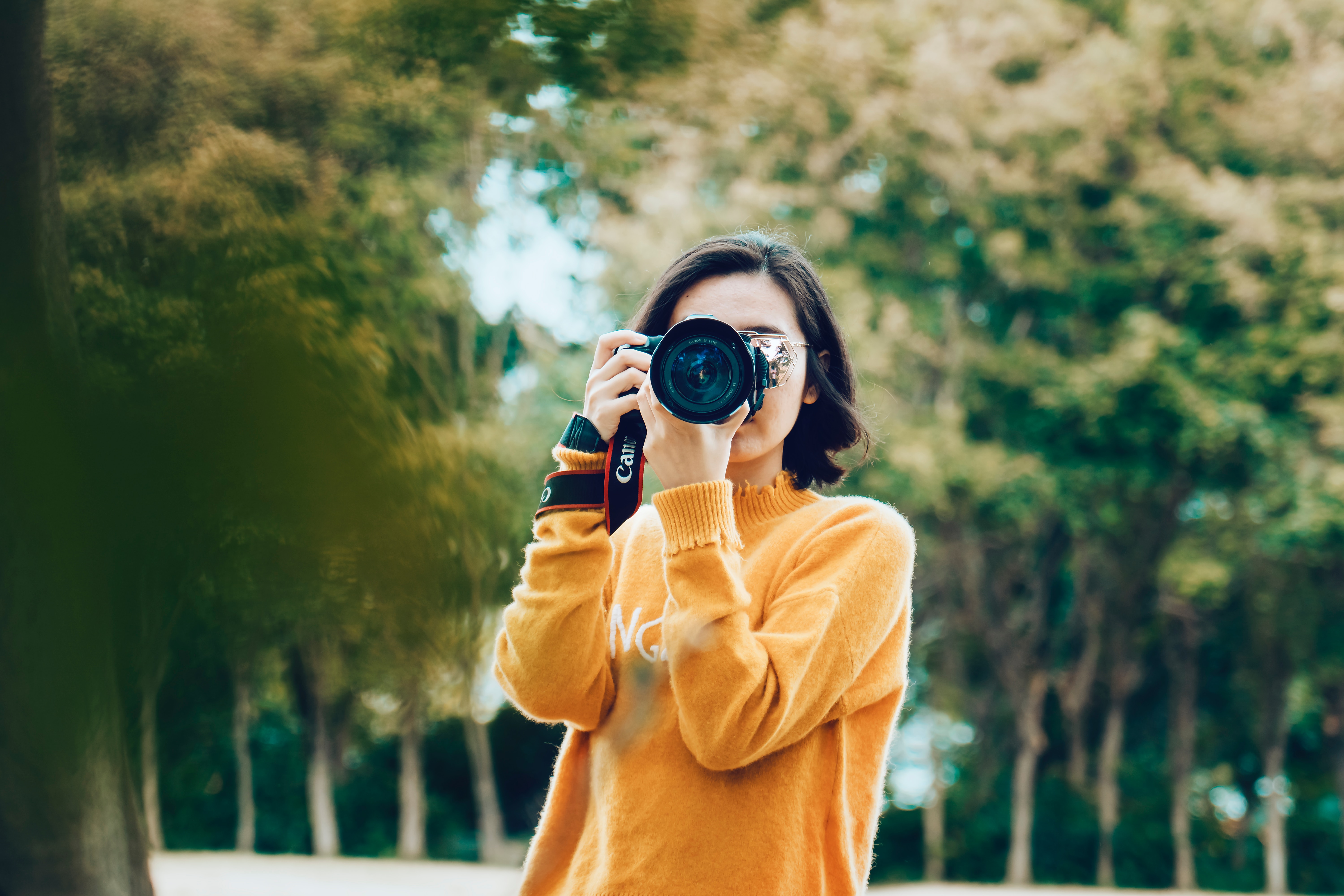Woman holding camera standing outside with trees